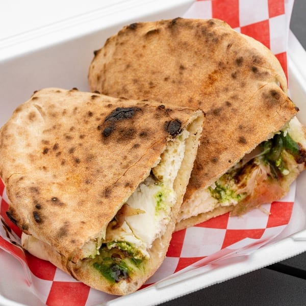 Two Captain's Pizza Company calzones, filled with cheese and pesto, in a white takeout container.