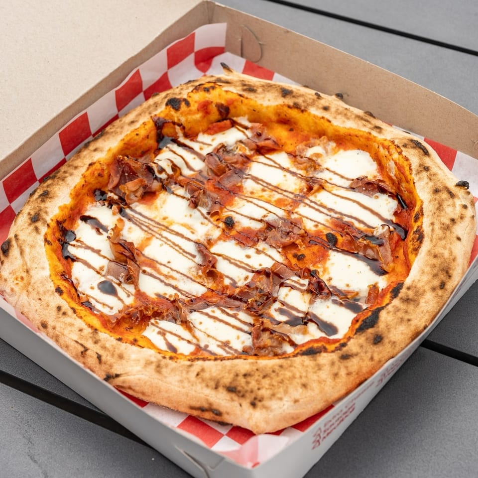 Captain's Pizza Company's pizza with mozzarella, tomato sauce, prosciutto, and balsamic glaze in a box.