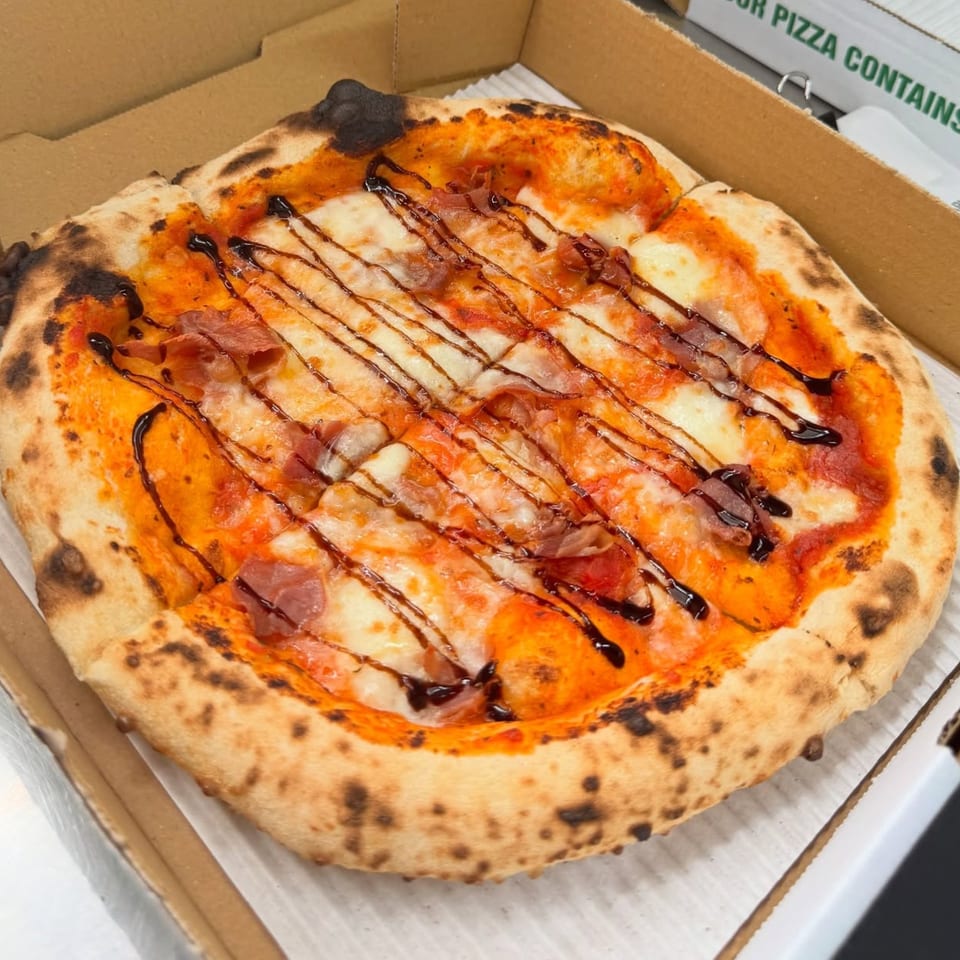 Captain's Pizza Company's pizza with prosciutto, mozzarella, and balsamic glaze in a delivery box.
