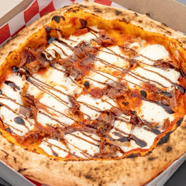 Captain's Pizza Company's pizza with mozzarella, tomato sauce, prosciutto, and balsamic glaze in a box.